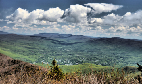 A panoramic view of a lush green valley surrounded by mountains under a partly cloudy sky.
