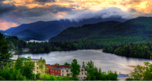 A serene lake surrounded by lush green mountains under a colorful sunset sky.