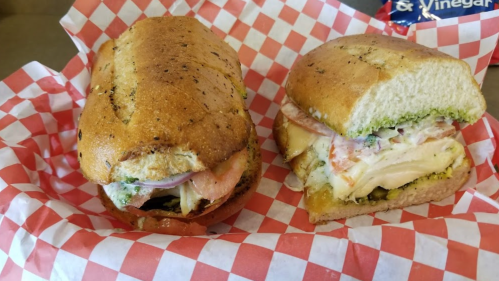 Two sandwiches on a red and white checkered paper, one cut in half, featuring various meats and toppings.