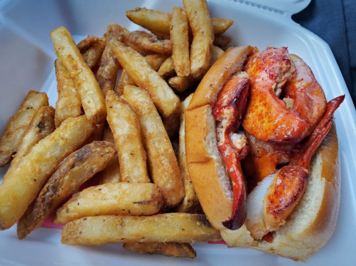 A lobster roll with chunks of lobster on a bun, served alongside a generous portion of golden, crispy fries.
