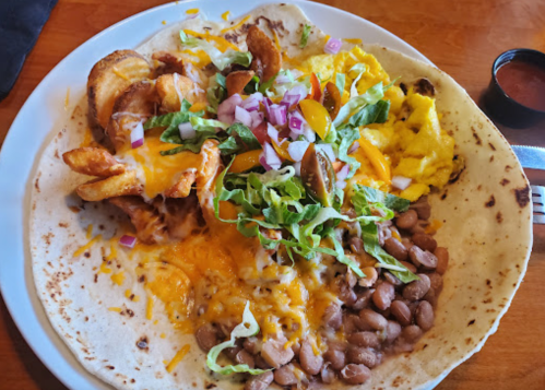 A large tortilla filled with beans, scrambled eggs, cheese, lettuce, and crispy potatoes, served with salsa on the side.