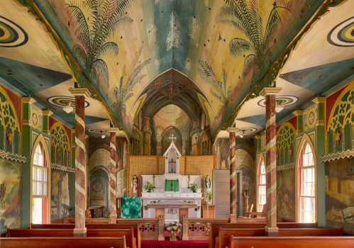 Interior of a colorful church featuring ornate murals, a central altar, and wooden pews.