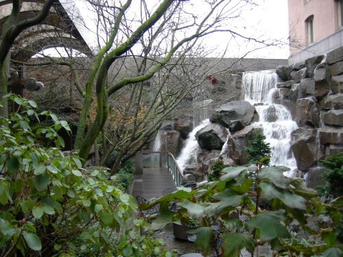 A serene waterfall cascades over rocks, surrounded by trees and lush greenery in a tranquil outdoor setting.