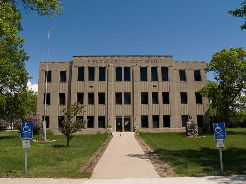 Sheridan County Courthouse, a modern building with a grassy area and accessible parking in front, under a clear blue sky.