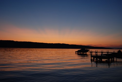 Silhouette of a dock at sunset, with vibrant colors reflecting on calm water and rays of light emerging from the horizon.