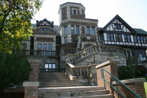 Historic mansion with intricate brickwork, large windows, and a grand staircase surrounded by greenery.