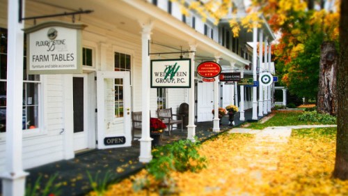 A charming storefront with signs for various businesses, surrounded by autumn leaves and colorful foliage.