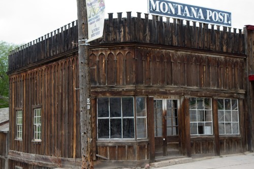 Historic wooden building with a sign reading "Montana Post," featuring a rustic design and large windows.