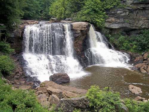 A scenic waterfall cascading over rocks into a serene pool, surrounded by lush greenery and rugged cliffs.