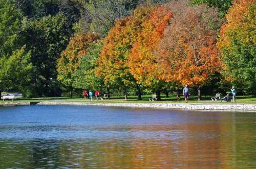 A serene park scene with colorful autumn trees reflecting in a calm lake, and people walking along the shore.