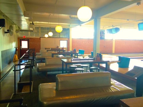 Interior of a bowling alley with seating, tables, and overhead lights, creating a casual atmosphere.
