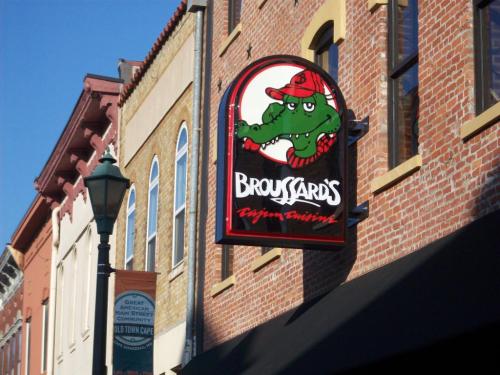 Sign for Broussard's Cajun Cuisine featuring a cartoon alligator wearing a red hat, mounted on a brick building.