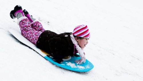 A child in winter clothing sleds down a snowy hill, focused and enjoying the ride.