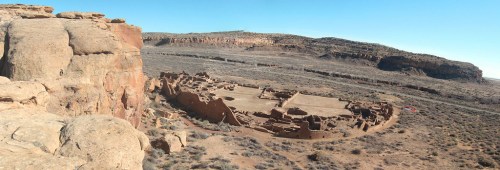 Panoramic view of ancient ruins surrounded by arid landscape and rocky cliffs under a clear blue sky.