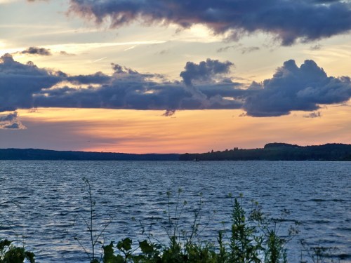A serene lake at sunset, with colorful clouds reflecting on the water and lush greenery in the foreground.