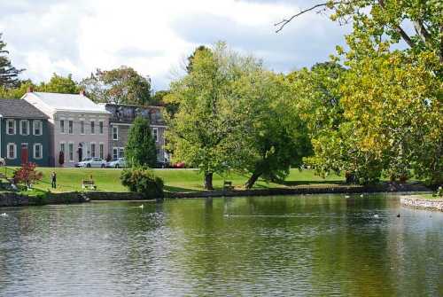 A serene lake surrounded by green trees and charming houses under a partly cloudy sky.