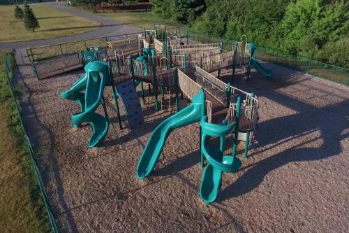Aerial view of a playground featuring multiple slides, climbing structures, and a gravel surface, surrounded by greenery.