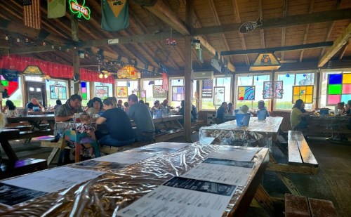 A bustling restaurant interior with colorful stained glass windows and diners seated at wooden tables.