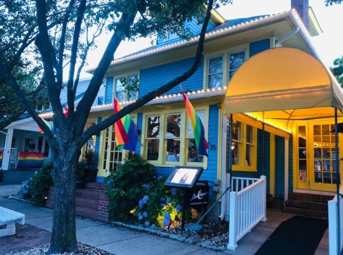 A colorful house with rainbow flags and a yellow awning, warmly lit in the evening.