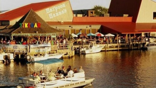 A lively waterfront scene with a restaurant, boats, and people enjoying the outdoor atmosphere at sunset.