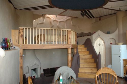 A cozy, artistic interior featuring a lofted bed, wooden stairs, and unique, curved walls.