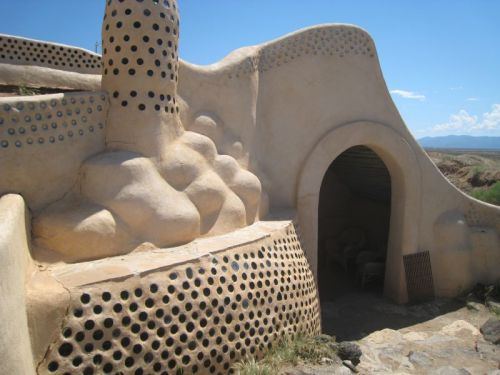 A unique, organic-shaped building with textured walls and circular openings, set against a clear blue sky.