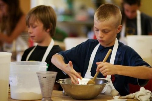 Two boys in aprons are mixing ingredients in a bowl during a cooking class, focused on their tasks.
