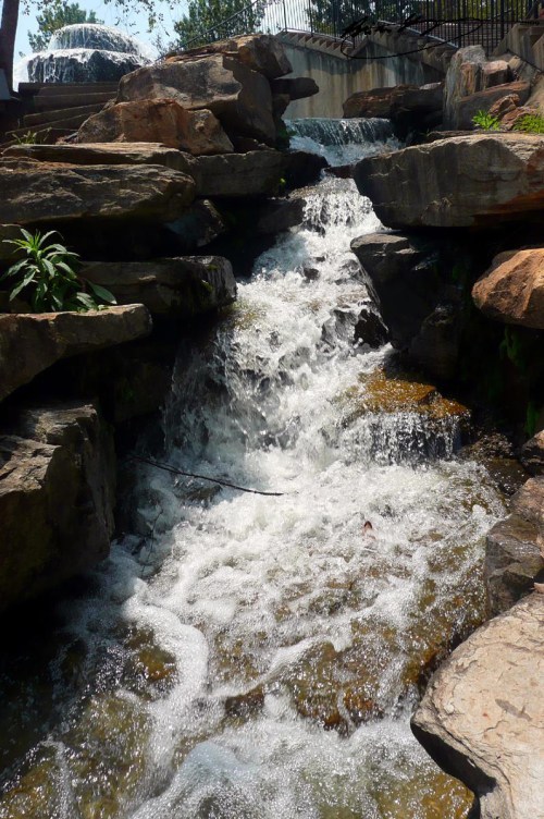 A cascading waterfall flows over large rocks, creating a serene natural scene with splashes of water.