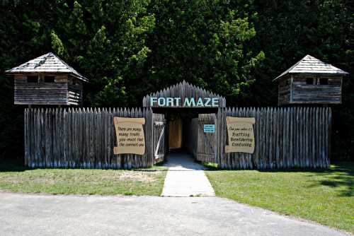 Entrance to Fort Maze, featuring wooden towers and a sign warning about multiple paths inside. Surrounded by greenery.