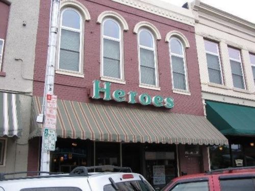 Sign for "Heroes" on a brick building with arched windows and a striped awning. Cars parked in front.