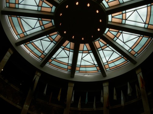 A circular skylight with geometric patterns and lights, viewed from below in a spacious interior.