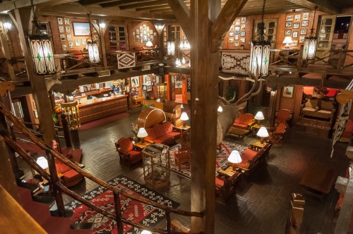 Cozy lodge interior with wooden beams, warm lighting, and a mix of seating areas and decorative photos on the walls.