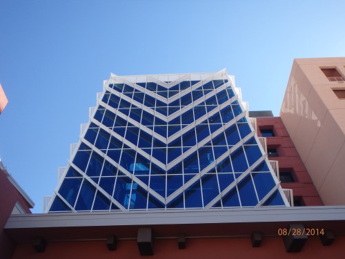 Modern building with a striking glass facade, featuring a chevron pattern against a clear blue sky.