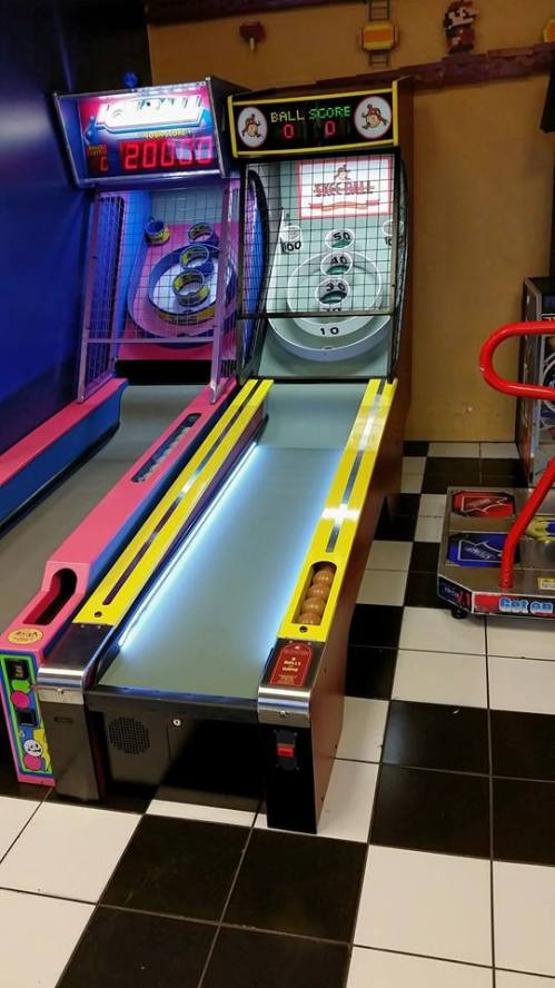 A brightly colored arcade game with a skee ball lane and score display, set in a game room with black and white tiles.