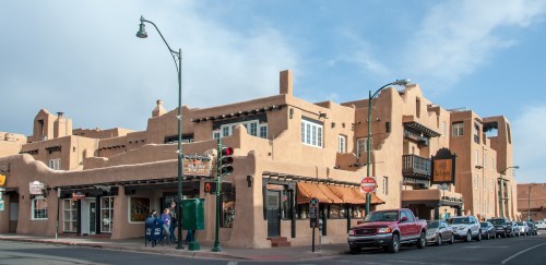 A southwestern-style building with adobe architecture, featuring shops and a traffic light on a sunny day.