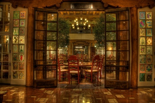 A warm, inviting restaurant interior with wooden doors open to a dining area featuring colorful decor and wooden chairs.