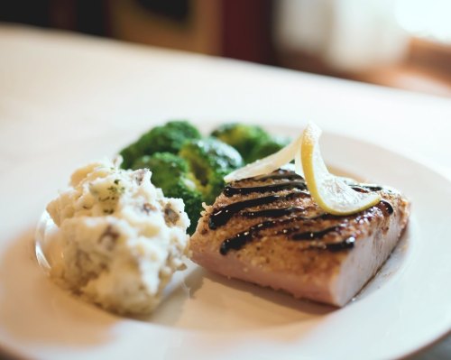 A plate featuring grilled fish with lemon, steamed broccoli, and creamy mashed potatoes.