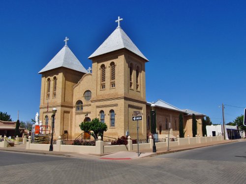Historic brick church with two towers and crosses, set against a clear blue sky, located at a street corner.