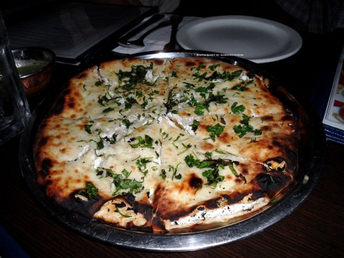 A round, freshly baked pizza topped with cheese and chopped herbs, served on a metal platter.