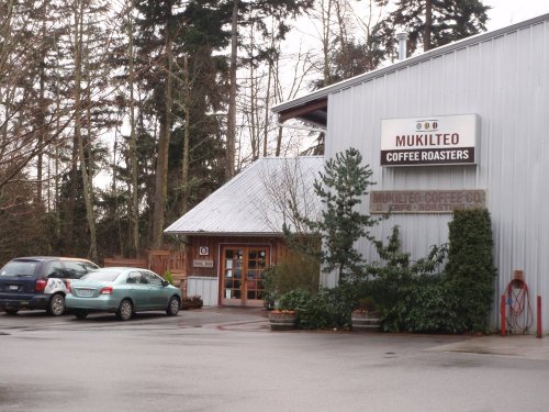 Exterior of Mukilteo Coffee Roasters with a parking area and trees, set in a wooded environment.