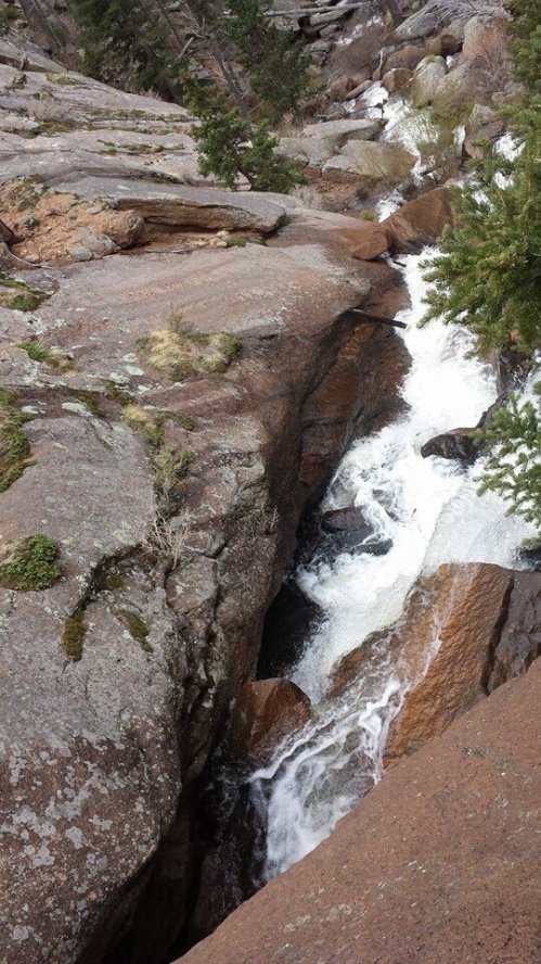 A cascading waterfall flows through rocky terrain, surrounded by trees and moss-covered stones.