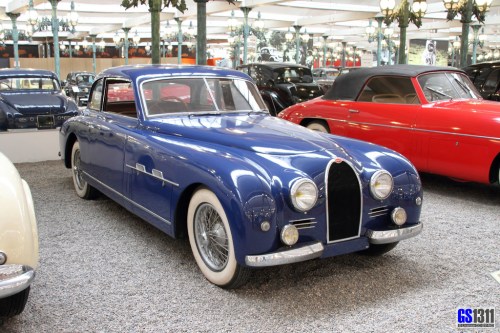 A vintage blue car with a sleek design, parked in a classic car museum surrounded by other vintage vehicles.
