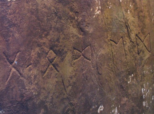 Ancient carvings on a textured rock surface, featuring a series of intersecting lines and symbols.