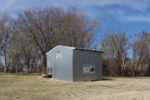 A small, blue metal building labeled "Cave" surrounded by trees and grass under a clear blue sky.