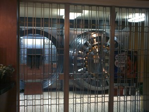 A large bank vault with a metal door, secured by bars, inside a bank setting.