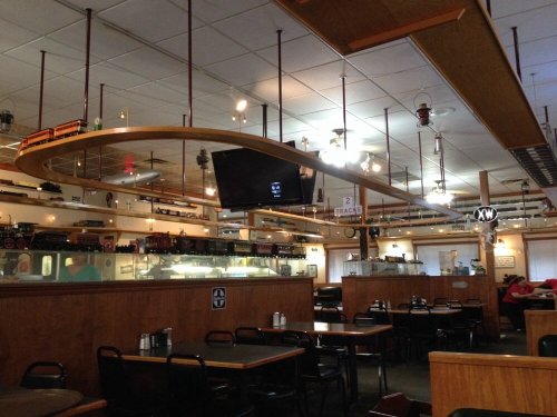 Interior of a diner featuring wooden tables, a curved ceiling design, and decorative train models on display.