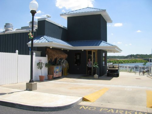 A blue-roofed building with a white fence, near a body of water, featuring potted plants and a "No Parking" sign.