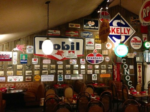 A cozy restaurant interior adorned with vintage gas station signs and memorabilia, featuring wooden walls and seating.