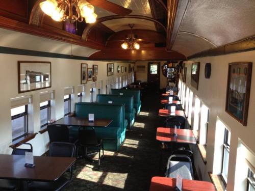 Interior of a vintage train dining car with green booths and tables, illuminated by natural light from windows.