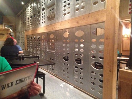 Interior of a restaurant featuring a metal wall with circular cutouts, wooden accents, and empty tables.